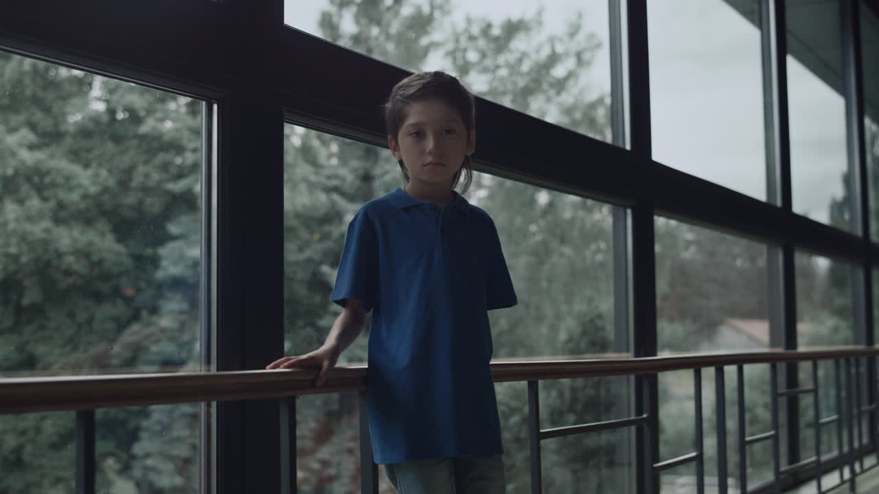 파노라마 창문 근처에서 혼자 포즈를 취하는 화가 난 학교 소년. 홀로 서 있는 소년 복도