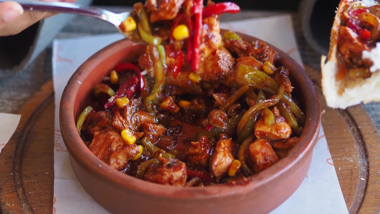 Persona che mangia pollo e verdure saltati da una pentola di terracotta