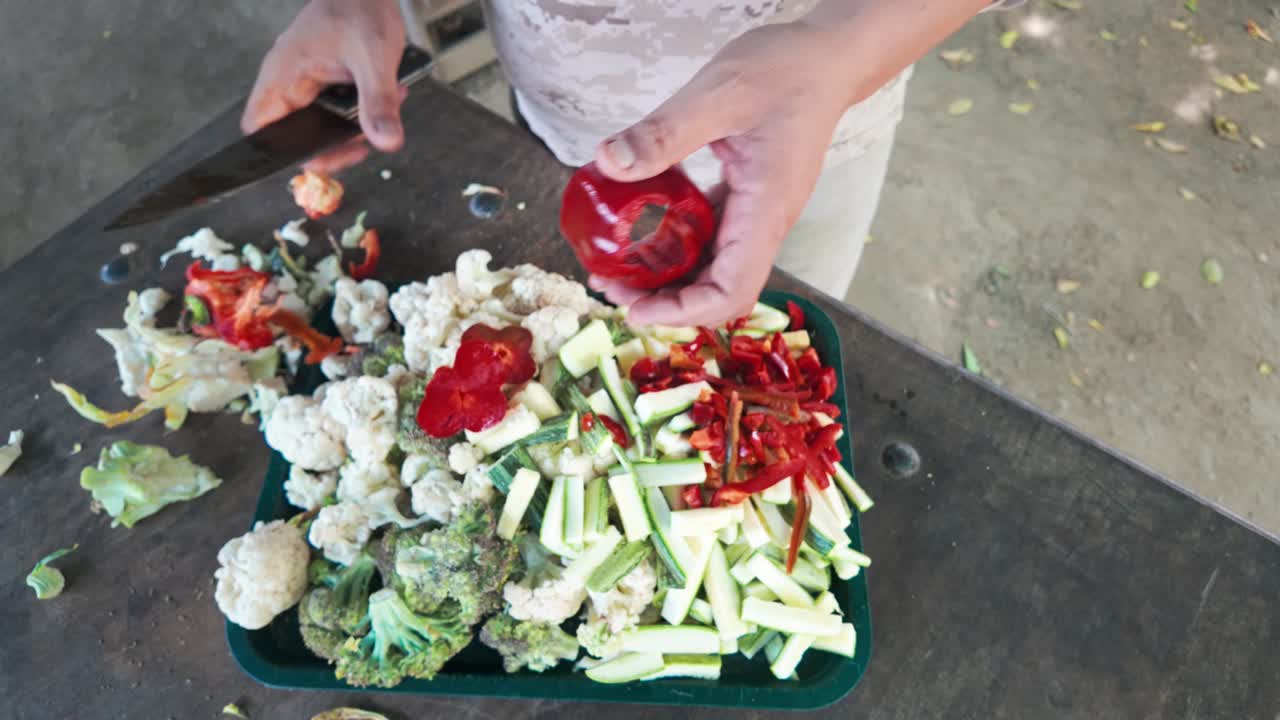 A person cutting vegetables by hand, including cauliflower, broccoli, and red chili