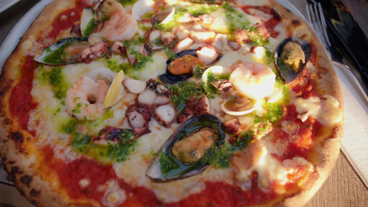 Appetitosa pizza ai frutti di mare con cozze, gamberi, polpo, vongole e pesto, che rappresenta la cucina italiana e la ristorazione gourmet.