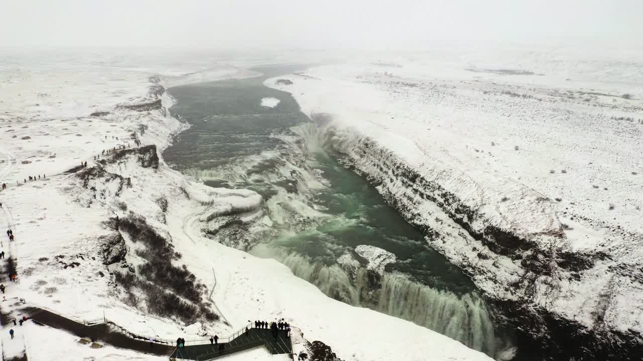 Stunning top-down view showcasing the powerful double-drop cascade of Gullfoss waterfall amidst snowy cliffs and icy waters.