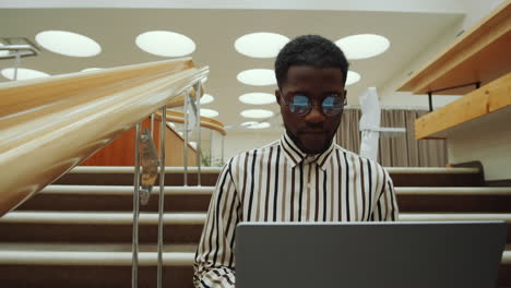african american man using laptop on library stairs