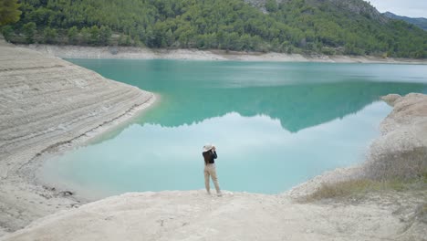 woman taking photo at turquoise lake surrounded by mountains
