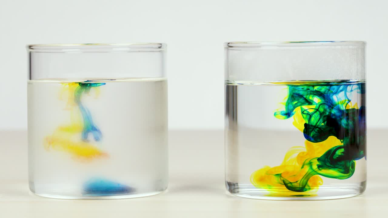 Colored dye disperses in two glasses of water, demonstrating temperature effects on diffusion speed