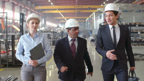 engineers in elegant clothes and helmets walking on corridor in a factory discussing details about business