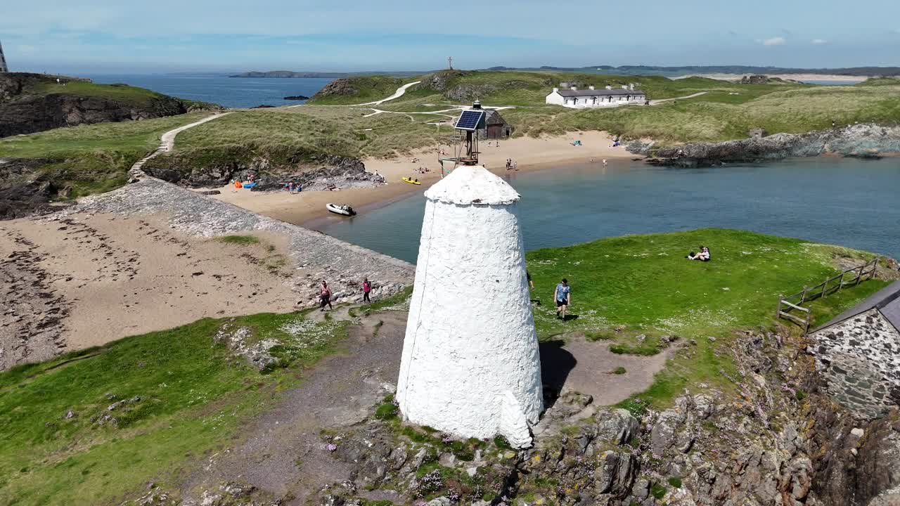 Drone captures tourists walking toward beacon on rocky coastline by sea in England, UK. with scenic ocean in background, creating picturesque and adventurous coastal experience
