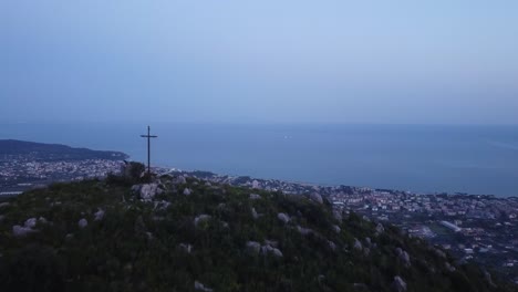 mountain top with cross and cityscape bellow on italy coast aerial drone reveal