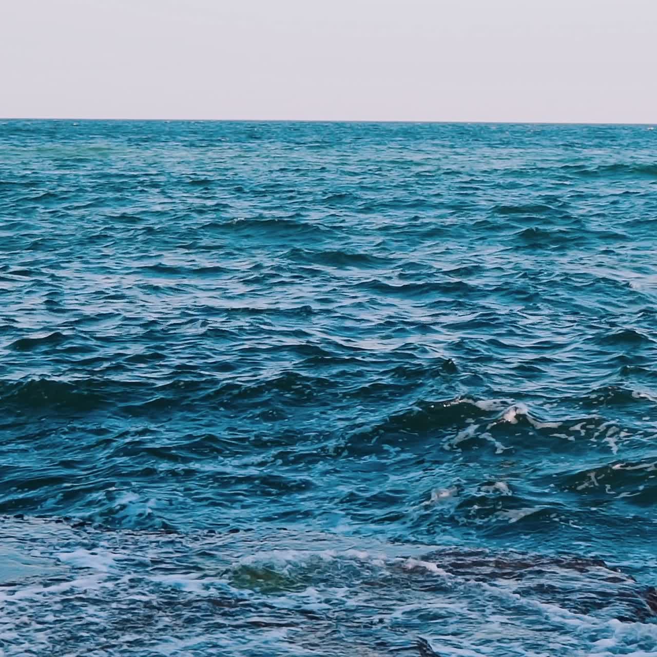 Waves crashing on stone beach. Amazing view of sea water. Blue water surface. Beautiful motion of sea water. Slow motion.