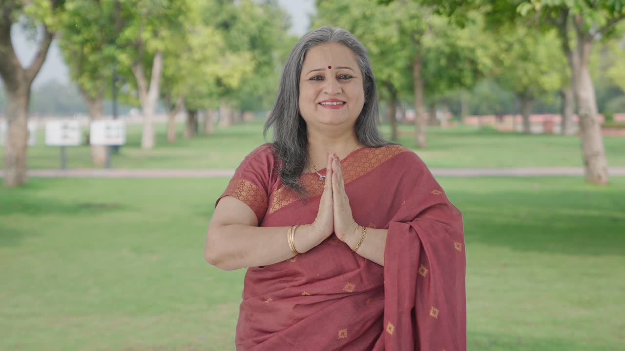 Felice anziana donna indiana che fa Namaste e saluta gli ospiti nel parco