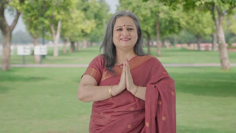 happy indian old woman doing namaste and greeting guests in park