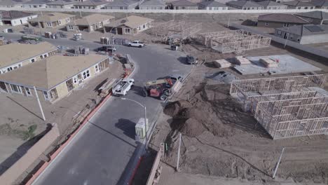 Un-Dron-En-Círculos-Captura-Una-Carretilla-Elevadora-Extensible-En-Acción,-Bajando-Suavemente-Una-Carga-De-Madera-En-El-Sitio-De-Construcción-De-Una-Casa-Dentro-De-Un-Nuevo-Vecindario.