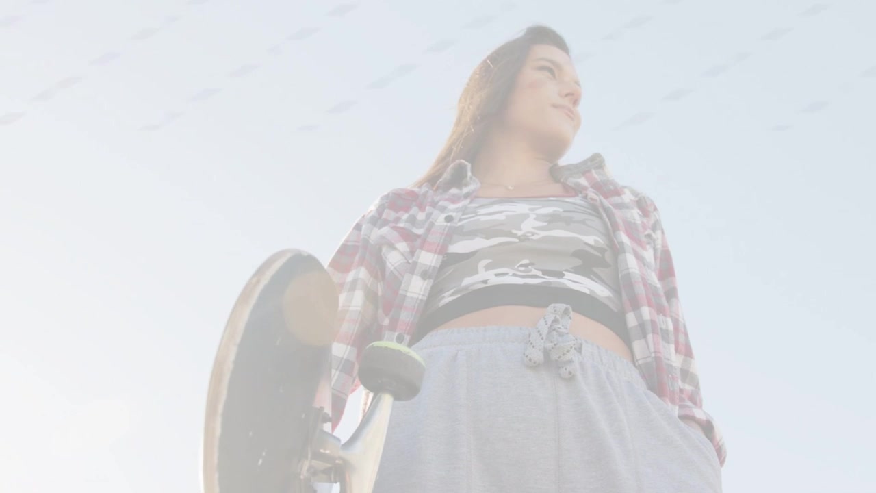 Female skater holding skateboard low under clear sky, lens flare reducing, revealing sports vibe