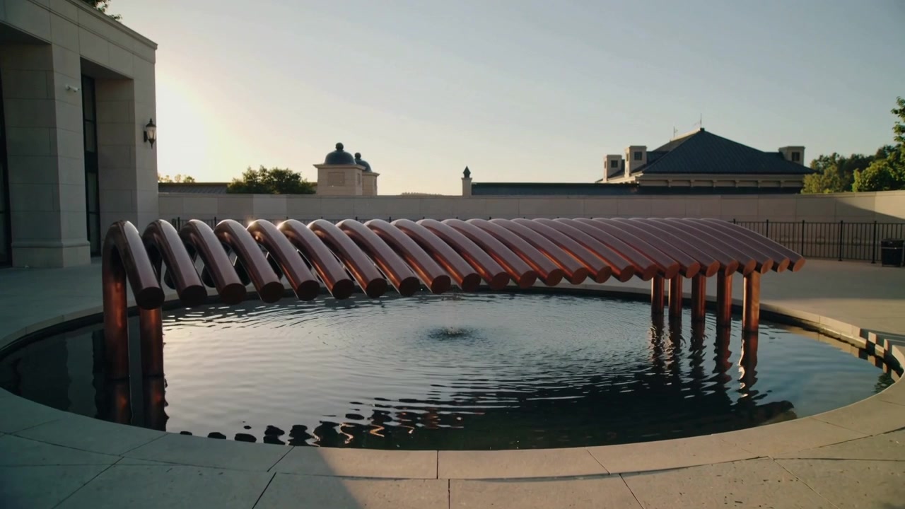 Una fuente crea un pulso enviando ondas a través de una piscina redonda en un patio, rompiendo el reflejo estriado.