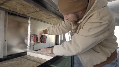 Carpenter-using-cordless-drill-to-create-a-shelf-indoors