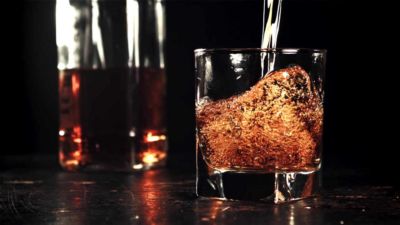 Versamento al rallentatore di whisky ambrato in un bicchiere.
