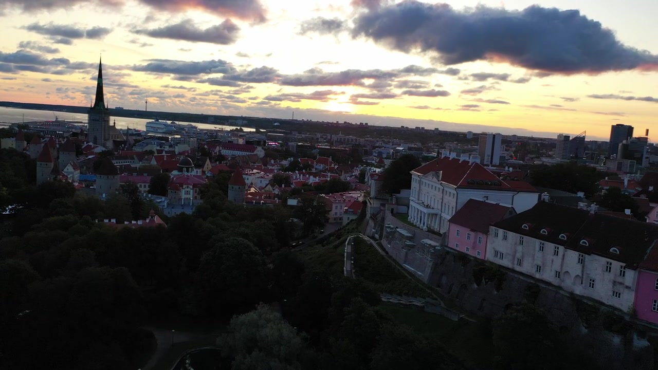 Filmato mozzafiato con drone del Centro Storico medievale di Tallinn al tramonto. L'inquadratura mostra la Collina di Toompea, la Cattedrale di Santa Maria e gli edifici dai tetti rossi sotto un cielo drammatico di nuvole rosa e arancioni.