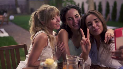 mujeres despreocupadas charlando en un café veranda al aire libre tomando una foto o video selfie en un teléfono inteligente