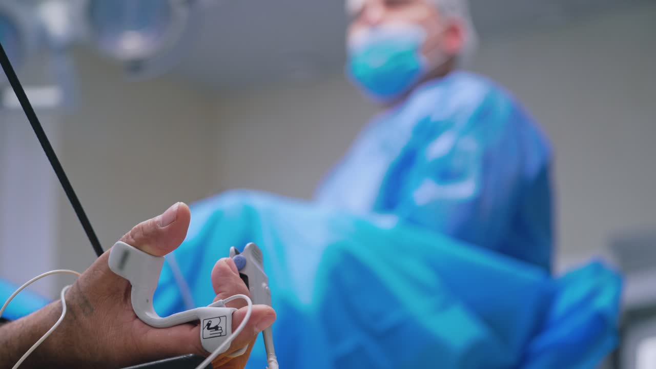Laparoscopic operation. Hand of a patient with many tubes. Close-up of man's hand during the operation on the blur background of a surgeon in clinic.