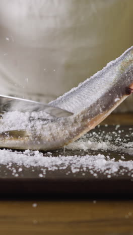 chef removes salt from delicatessen herring fish with large sharp knife on wooden cutting board at table closeup. healthy nutrition of seafood