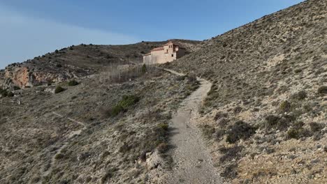 hermitage approaching drone view following a path in an arid desolate landscape in albarracin village, teruel, spain