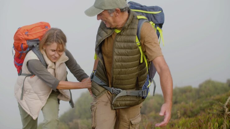 Senior man holding wife's hand and helping her to climb the mountain