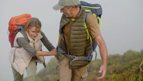 Senior-man-holding-wife's-hand-and-helping-her-to-climb-the-mountain