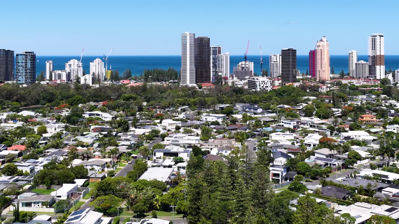 Daytime drone ascends above canal, residential area, and city skyline with clear blue sky