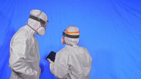 científico virólogo en respirador hace escribir en una tableta con lápiz. hombre y mujer con máscara médica protectora. clave de croma azul