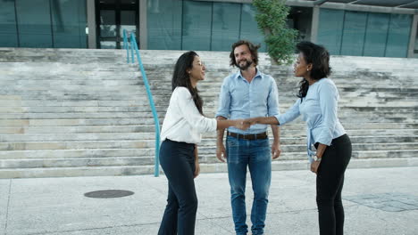 joven barbudo y su colega sonriendo y estrechando la mano con el solicitante de empleo en la calle