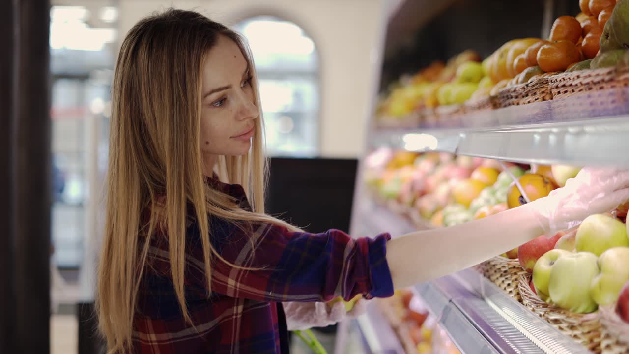 mujer con guante recoge frutas manzanas en la cesta en el supermercado