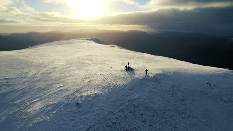 Antenne-über-Der-Silhouette-Der-Gruppe-Auf-Dem-Schneebedeckten-Arkle-Mountain-Im-Schottischen-Hochland-Gegen-Goldgelbes-Sonnenlicht