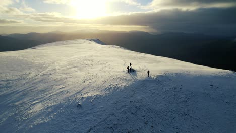 aerial over silhouette of group on snow covered arkle mountain in the scottish highlands against golden yellow sunlight