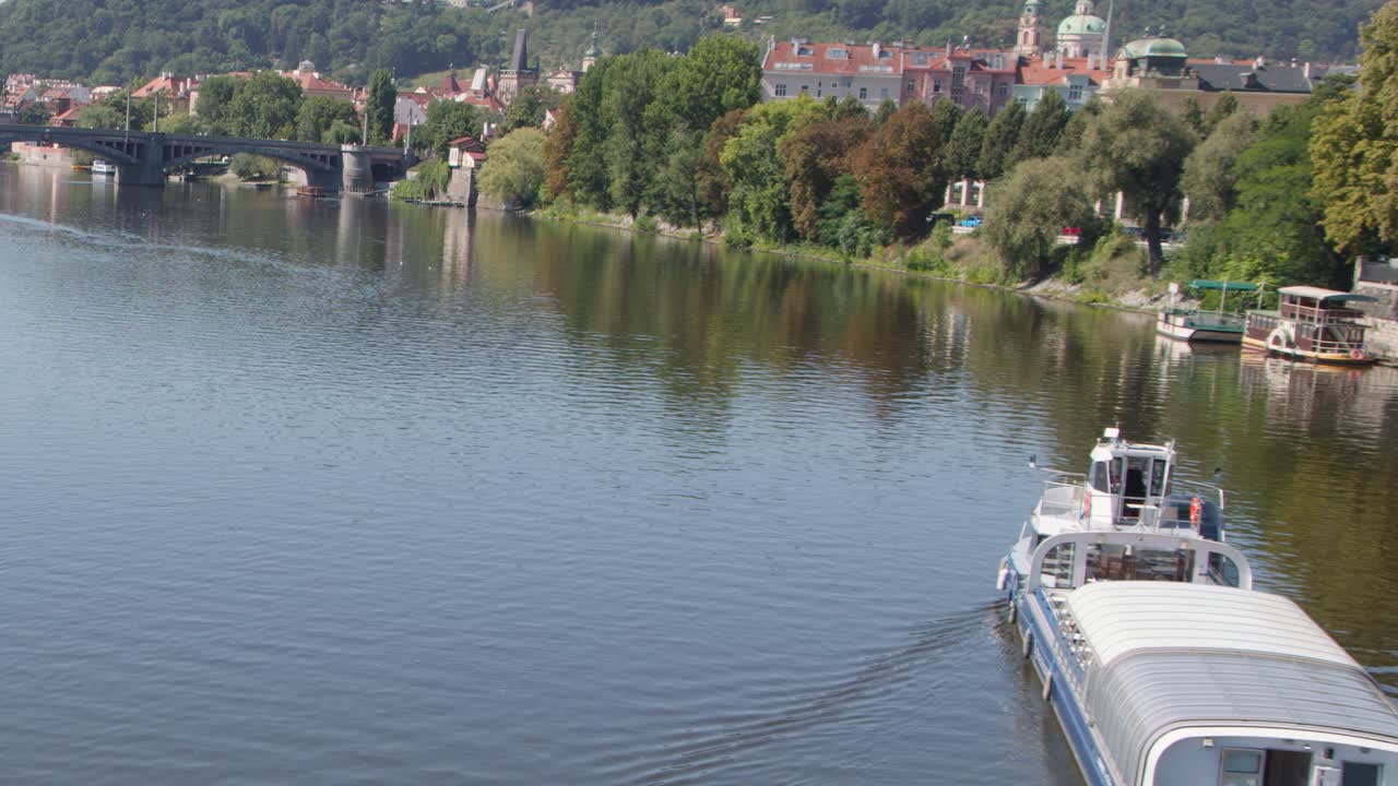 Passenger boat travels along Vltava River, Prague, under bright daylight with steady camera view
