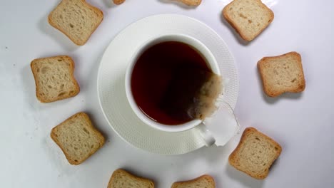 cup of tea with tea bag and a lot of white crispy crackers rotates slowly on a light background.