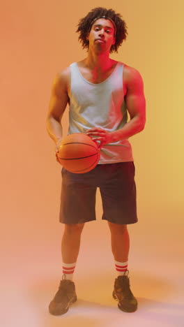video vertical de un jugador de baloncesto masculino biracial con una pelota en un fondo naranja