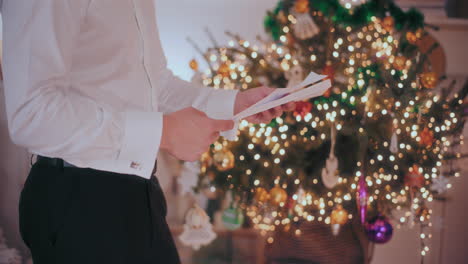 hombre abriendo una carta con un árbol de navidad decorado en el fondo