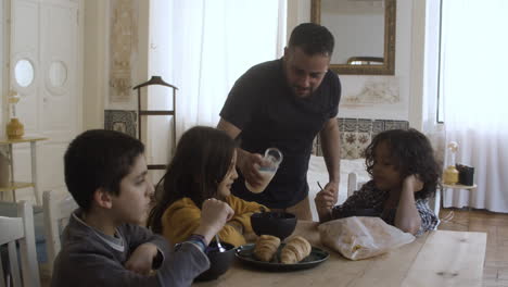 solicitous caucasian father pouring milk into kids plates.