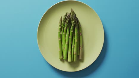 video of fresh asparagus on green plate over blue background