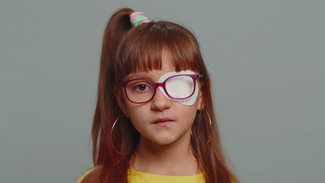 sick ill preteen girl looking at camera having protective bandage plaster patch scratch on one eye