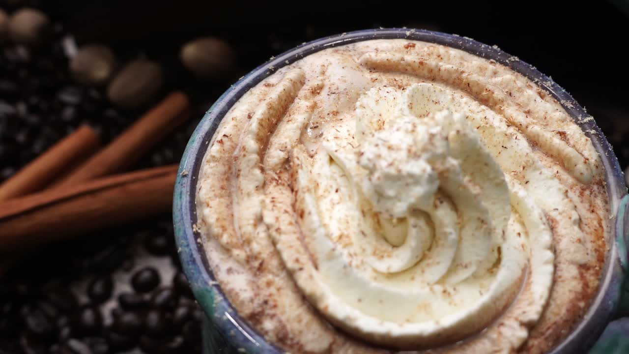 Cup or mug of coffee in a blue ceramic cup with whipped cream and a dash of nutmeg or cinnamon. Coffee beans surrounding a cozy cup of coffee in a blue mug.