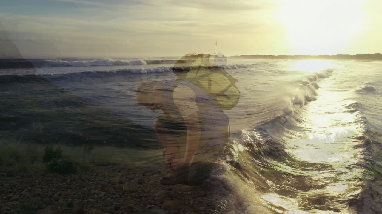 Male hiker kneeling on pebble beach at sunset, showing animated heart rate chart for health