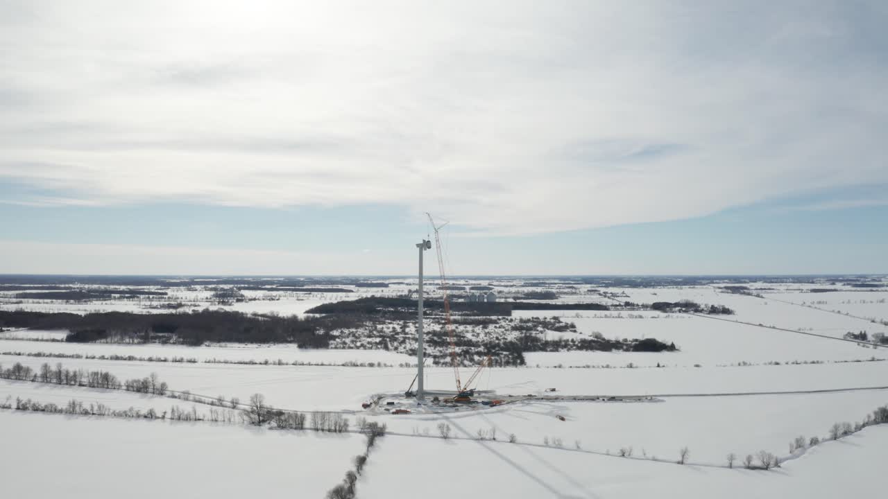 molino de viento gigante en construcción en invierno con paisaje nevado y grúa naranja alta