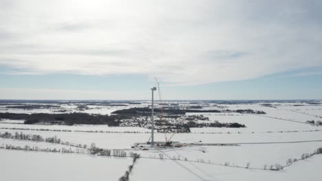 giant windmill under construction in winter with snowy landscape and tall orange crane