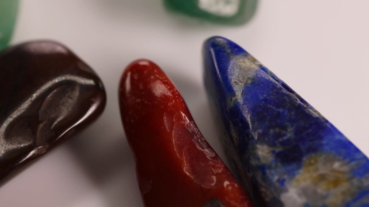 Vibrant chakra stones, including lapis lazuli and red jasper, spin gracefully on a white surface under soft lighting