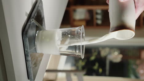 vertical video pouring vegan milk on ice into glass cup with glass straw in slow motion close up