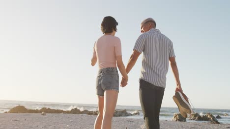 Glückliches-Gemischtrassiges-Paar,-Das-Am-Strand-In-Zeitlupe-Spaziert-Und-Händchen-Hält