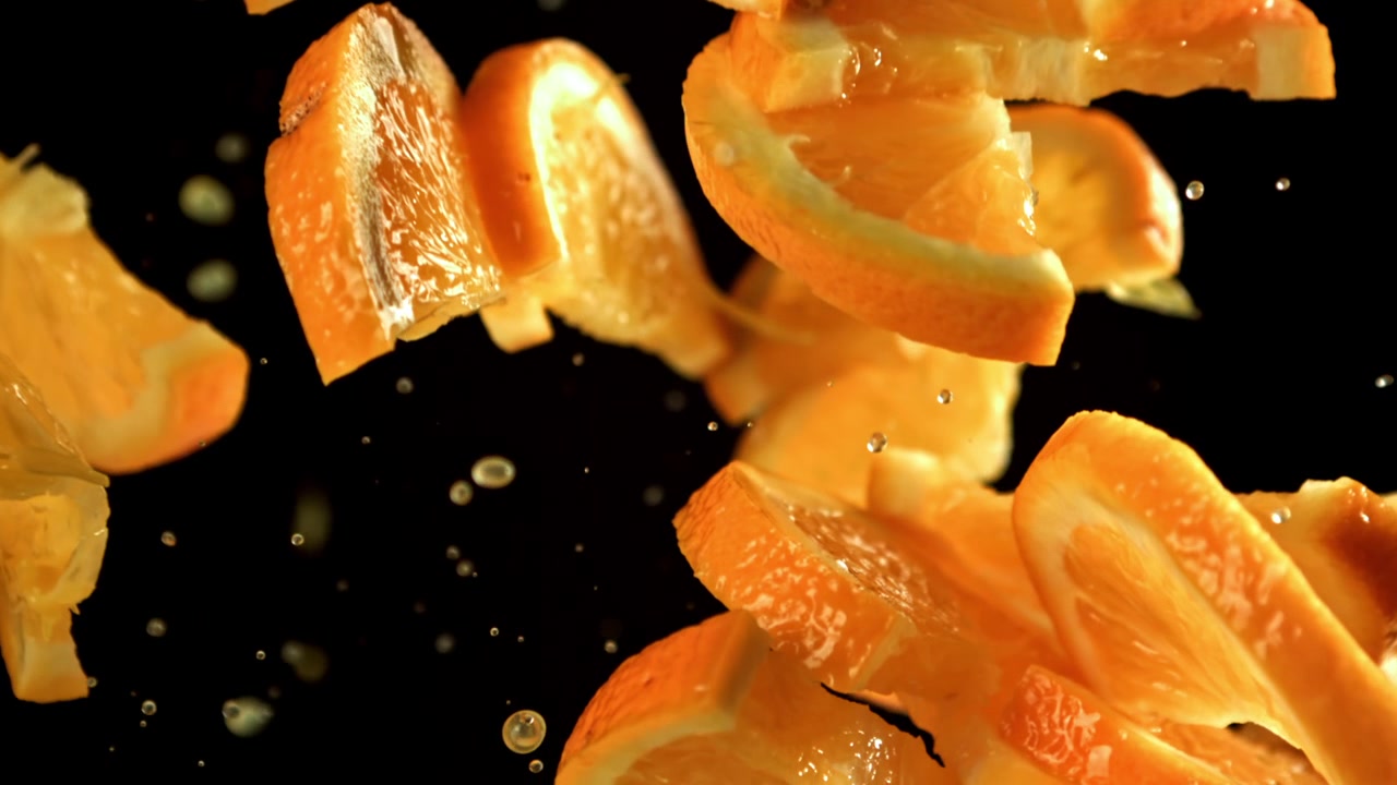 Fatias de laranja frescas e gotas de suco caindo em câmera lenta