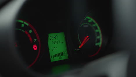 close up view of instrument cluster showing speedometer, tachometer and digital display lit in red and white, odometer reading and warning light icons visible through steering wheel blur