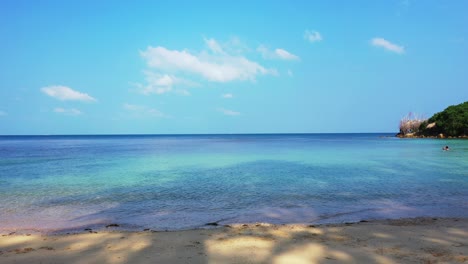 peaceful seascape with calm clear water of shallow lagoon under shadow of palm trees, bright sky with frozen white clouds, antigua