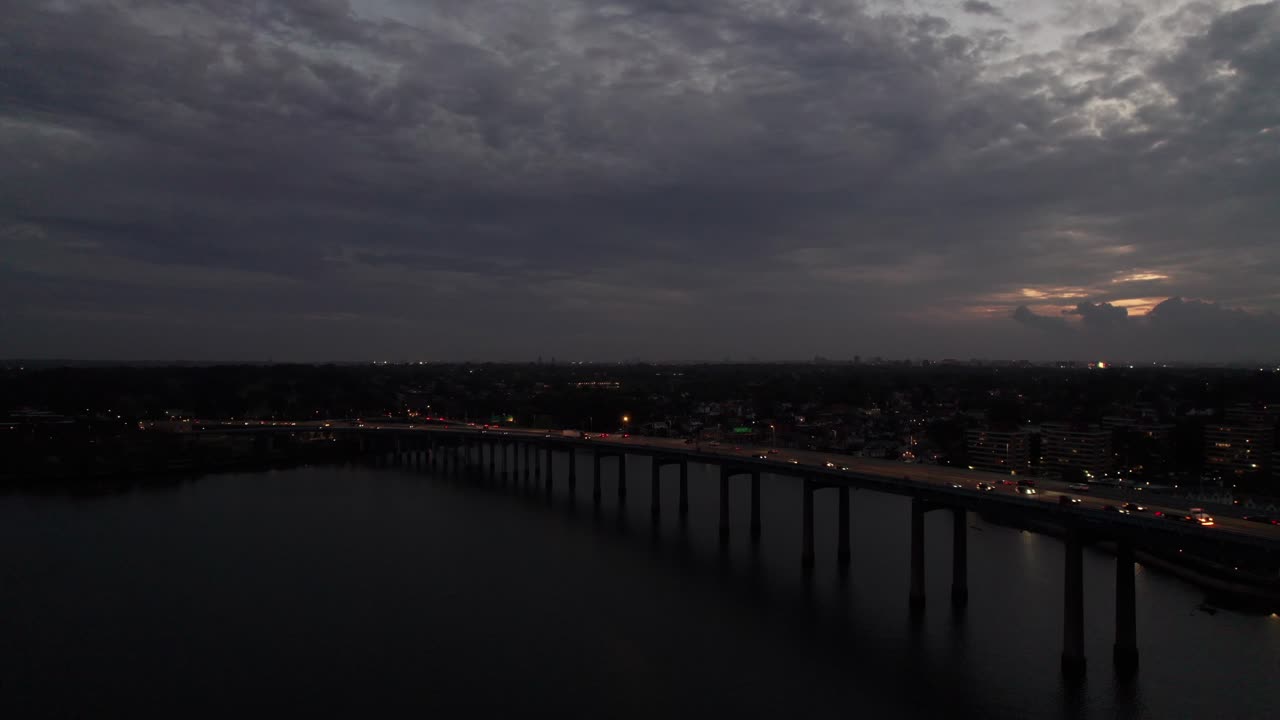 Headlights and vehicle traffic on causeway over water, New York City night drone shot, 4K